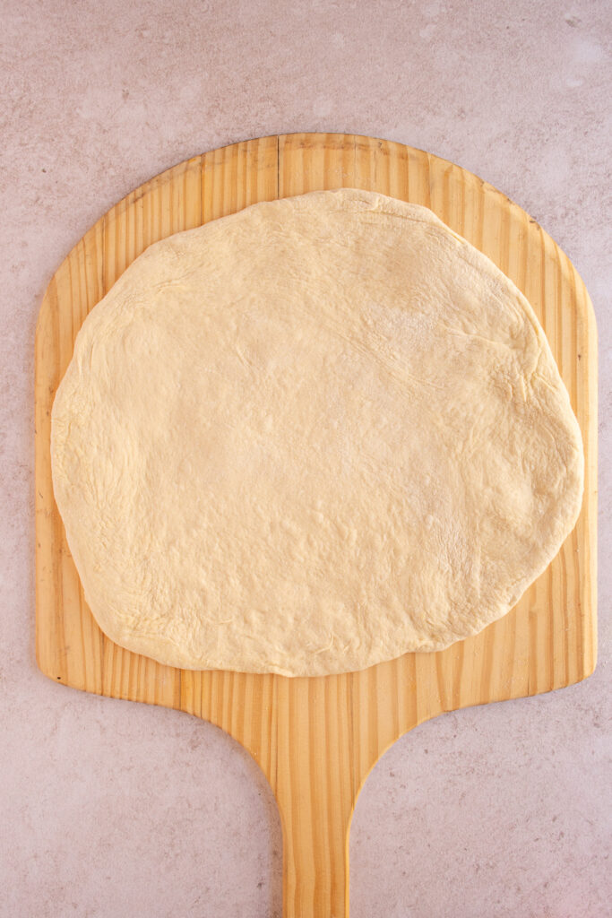 Pizza dough in a circular shape on a wood pizza peel.