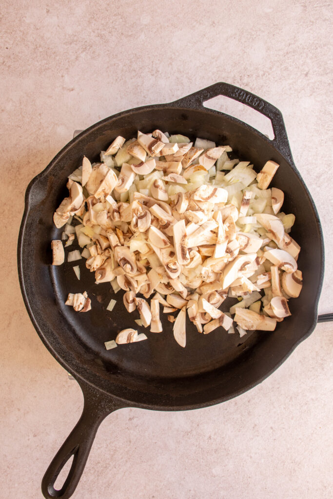 Adding mushrooms and diced onions to a large skillet.