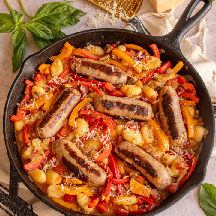 A large skillet with red and yellow bell peppers, gnocchi, and sausages.