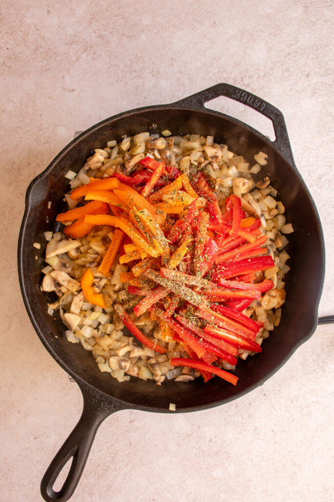 Adding red and yellow bell peppers to a skillet with onions and mushrooms.