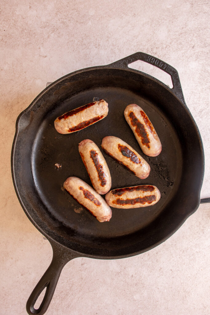 Browning sausages on a large black skillet.