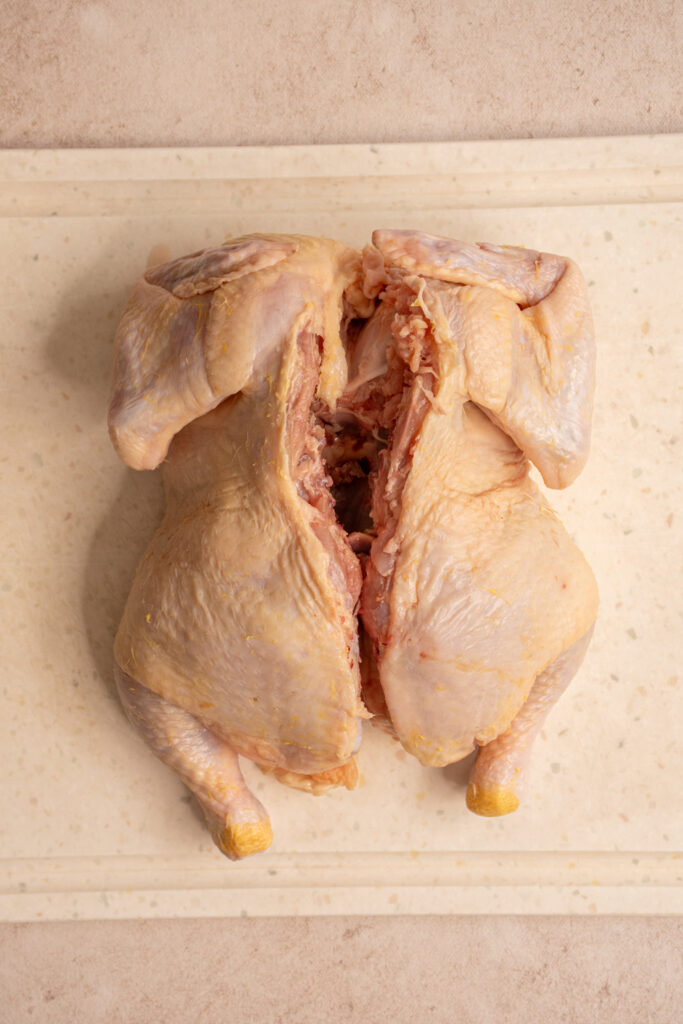 The backbone cut out of a whole raw chicken on a cutting board.