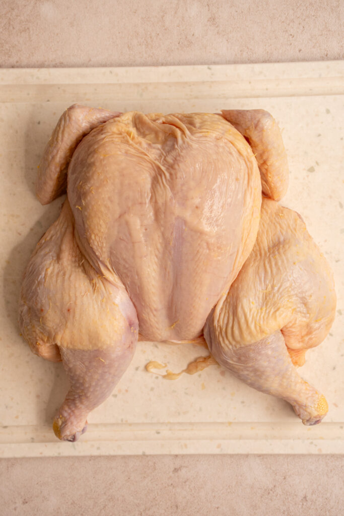 A fully spatchcocked chicken raw on a cutting board.