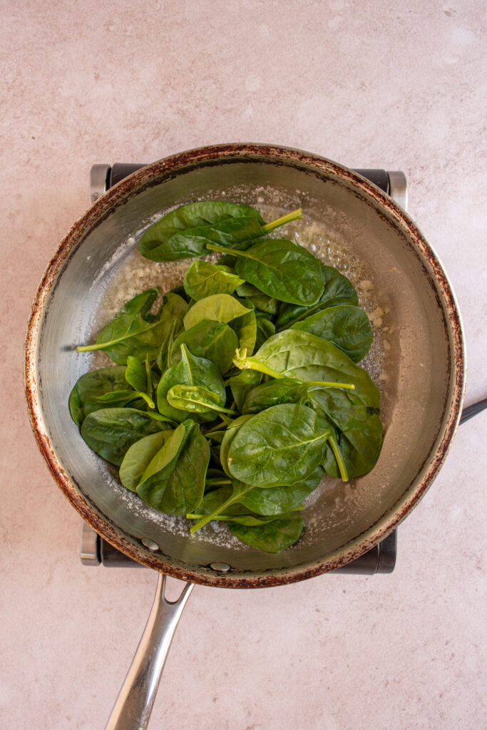 Fresh baby spinach added to a skillet.