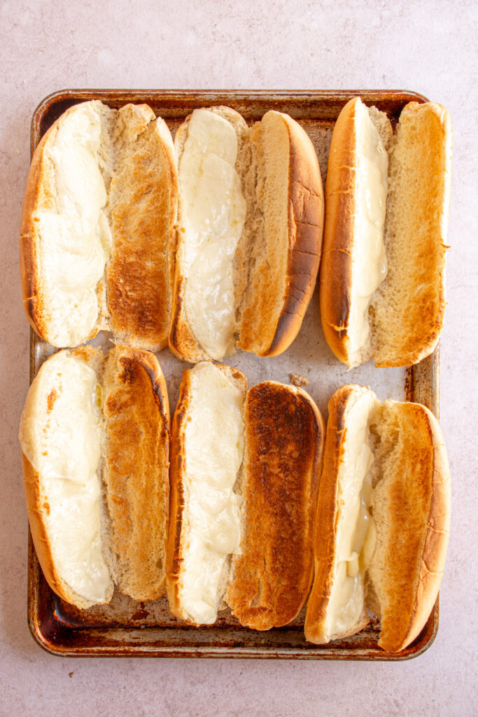 A sheet pan with toasted buns and melted cheese for sandwiches.