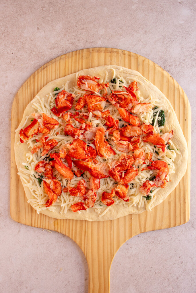 Uncooked lobster pizza piled high with lobster meat.