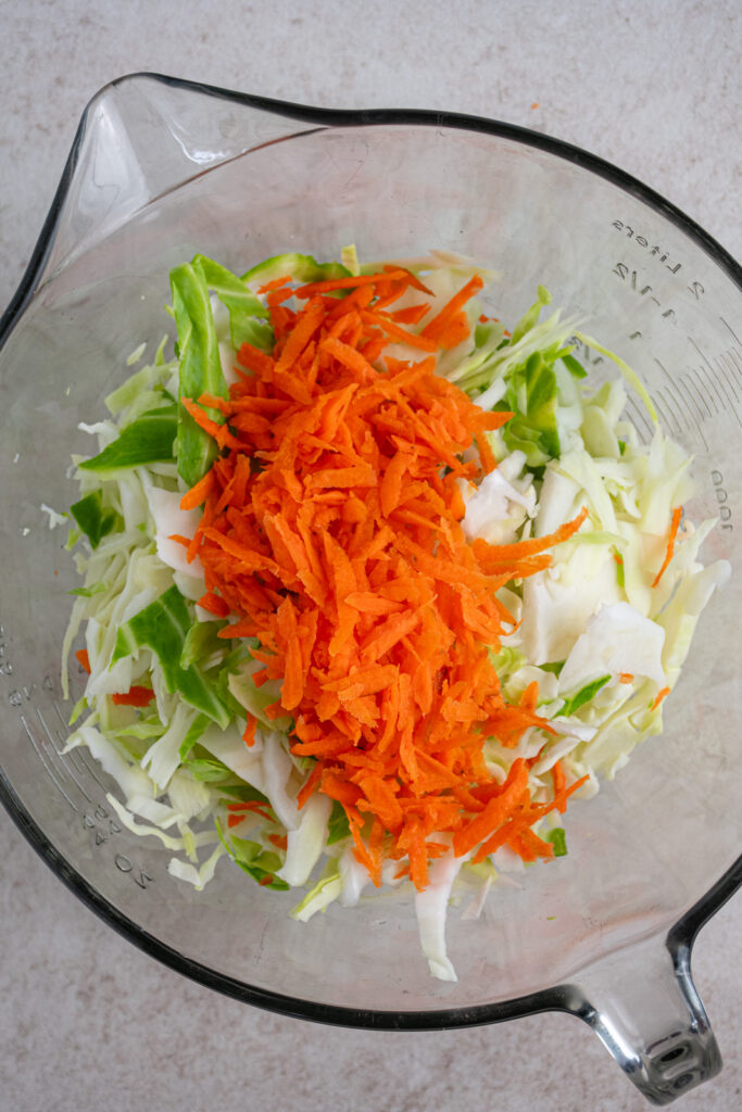 Cabbage and carrots shredded in a mixing bowl.