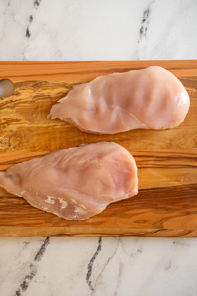 Two large chicken breasts on a cutting board.