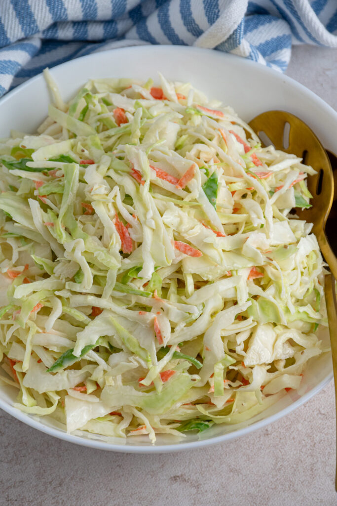 A large white serving bowl filled with green coleslaw recipe without celery seed.