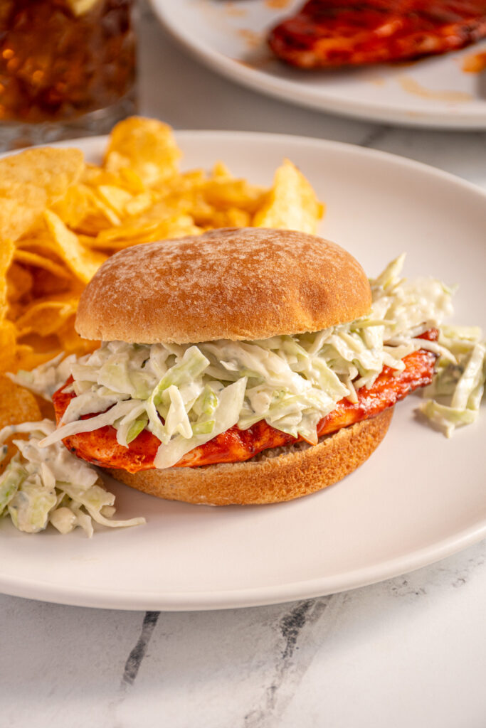 A grilled buffalo chicken sandwich topped with blue cheese coleslaw on a white plate.