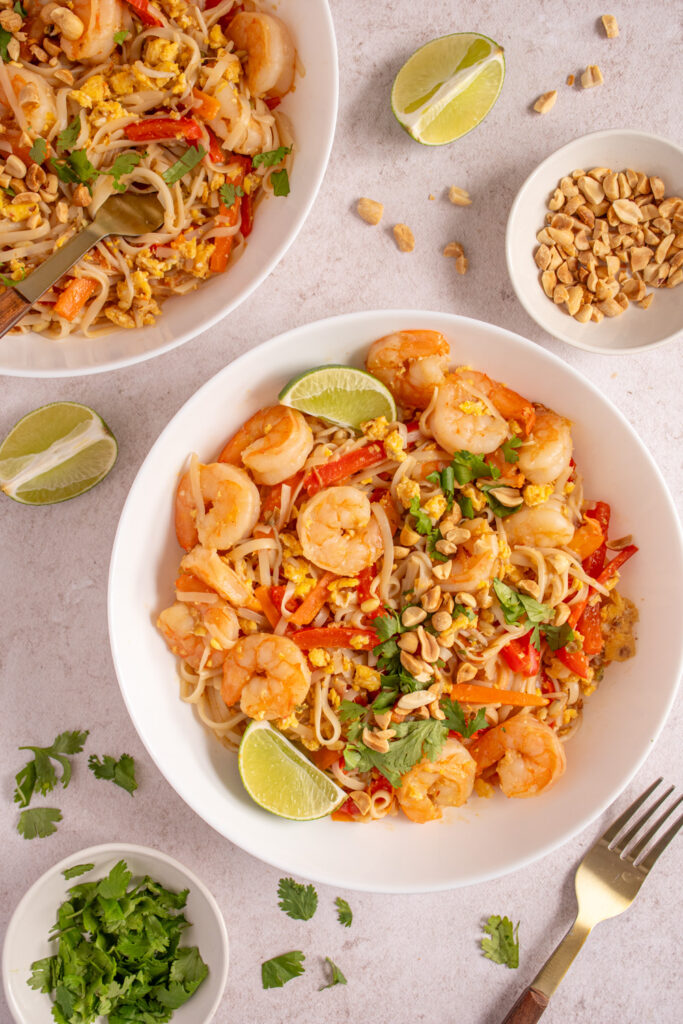 Overhead view of white bowls filled with shrimp pad thai and garnished with cilantro and chopped peanuts.