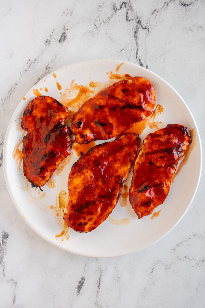 a white plate with very saucy grilled buffalo chicken cutlets.