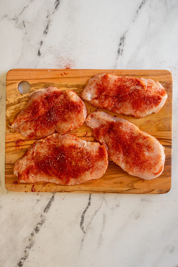 Seasoned chicken cutlets on a cutting board.