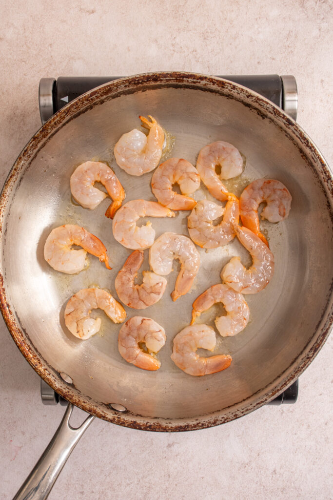 Raw shrimp added to a skillet.