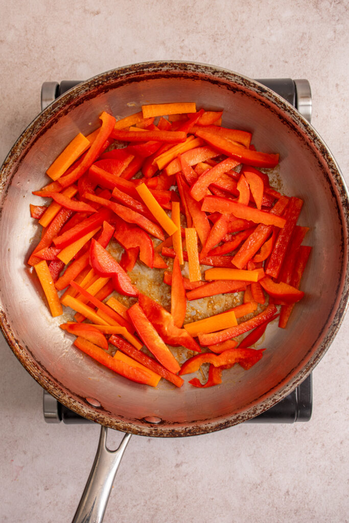 Fresh red bell pepper and carrots added to a skillet.