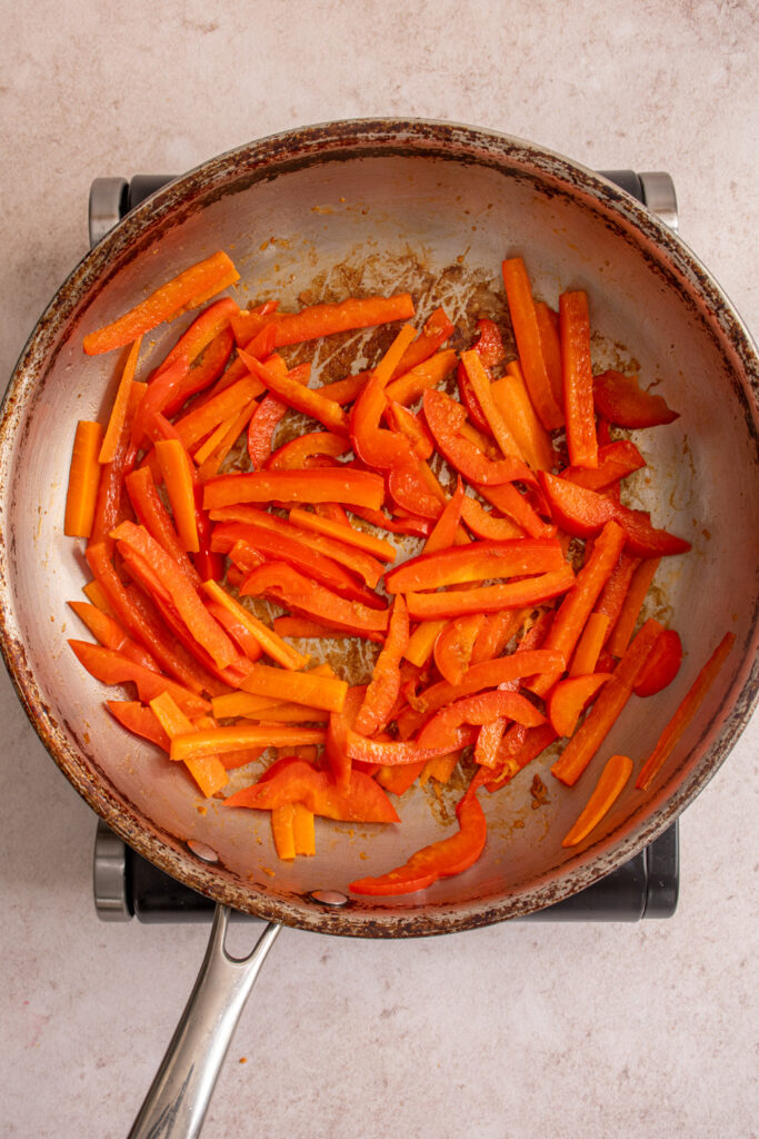 Cooked red bell pepper and carrots in a skillet.