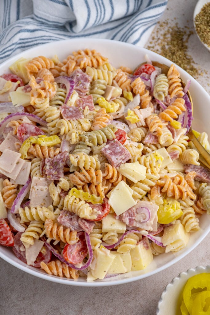 A white bowl filled with italian sub grinder pasta salad filled with deli meats, cheese, and vegetables.