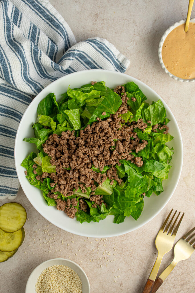 A white salad bowl filled with chopped romaine lettuce and browned ground beef.