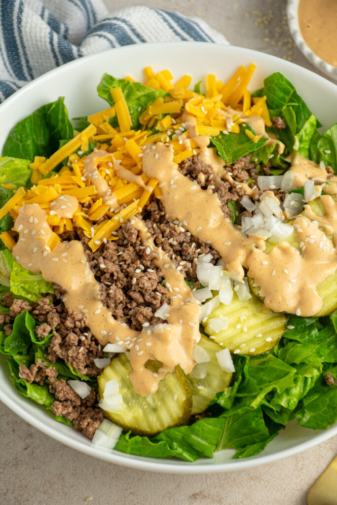 Close up of a big mac salad in a white serving bowl with big mac sauce on top.