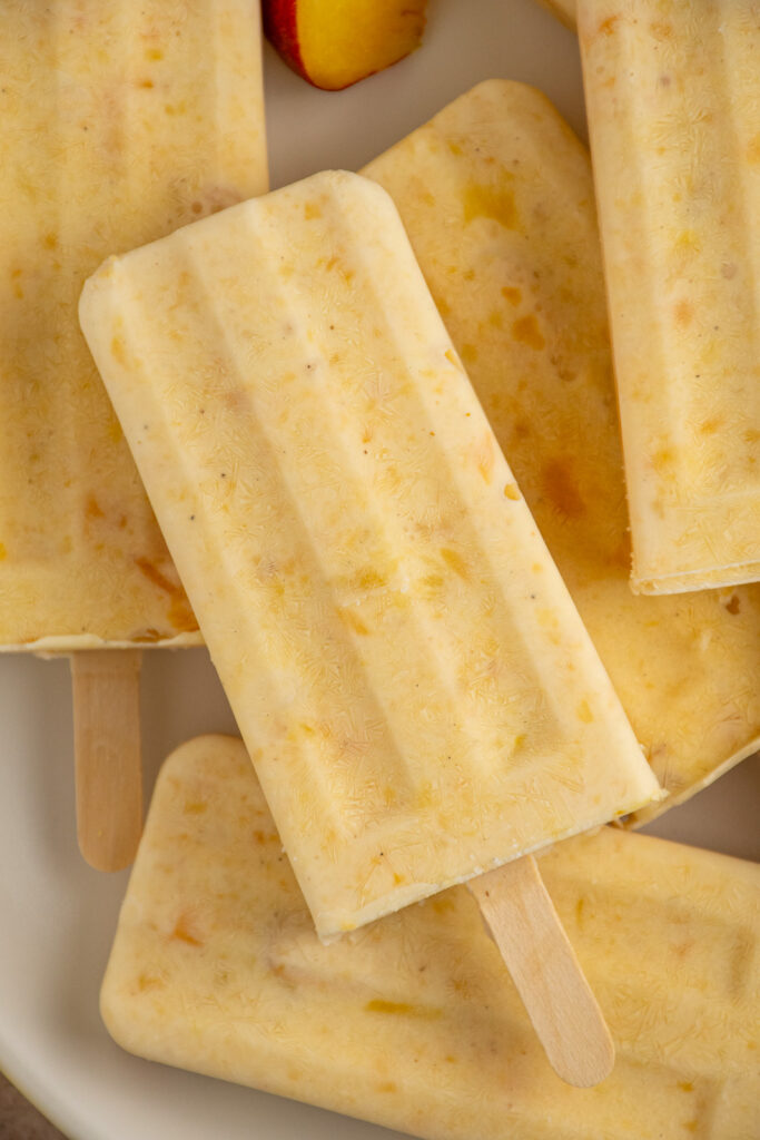Close up of a frozen peach yogurt popsicle on a pile of other popsicles.