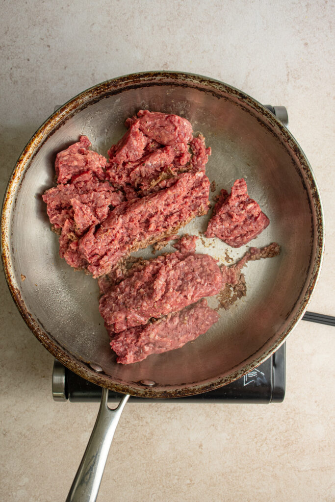 A large skillet with pink ground beef.
