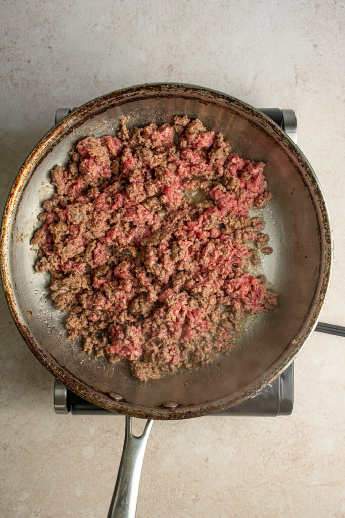 A large skillet with partially cooked ground beef.