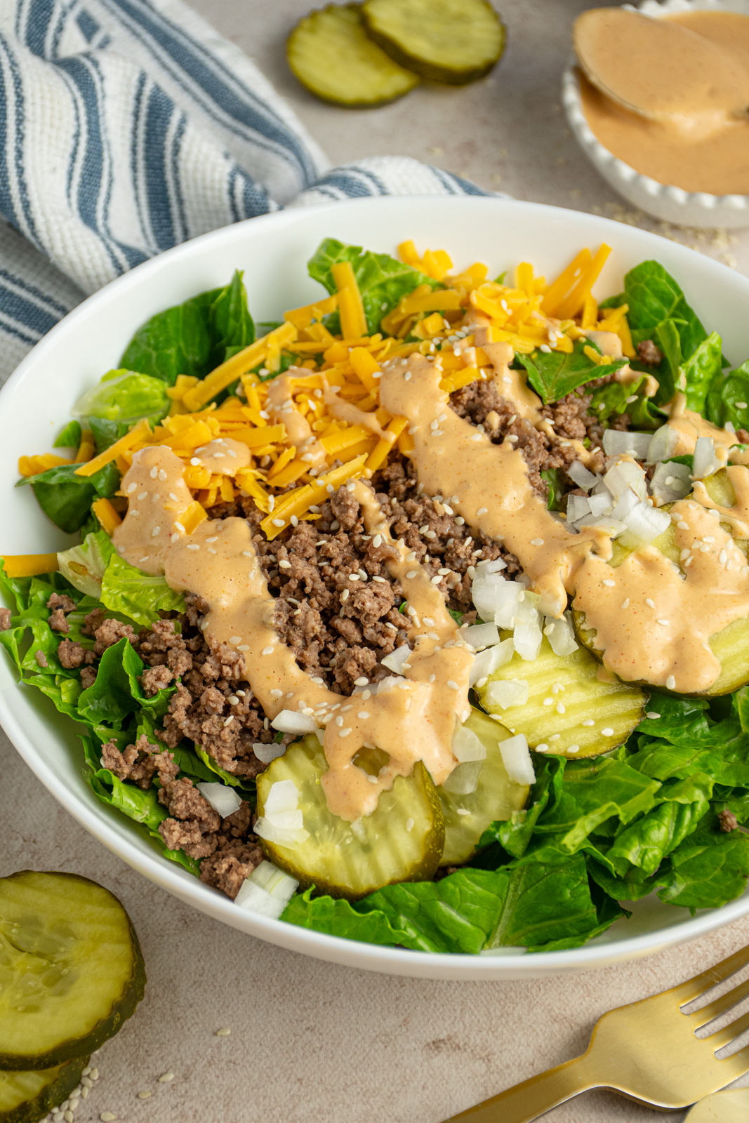 A white bowl with big mac salad with ground beef, cheese, pickles, and big mac sauce.