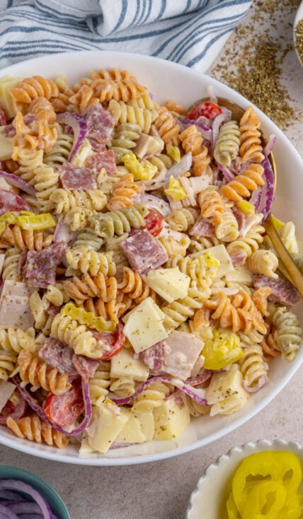 A large white bowl filled with colorful grinder pasta salad filled with deli meats, cheeses, and veggies.