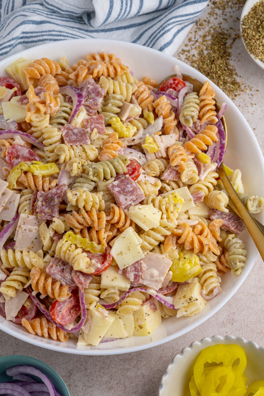 A large white bowl filled with colorful grinder pasta salad filled with deli meats, cheeses, and veggies.