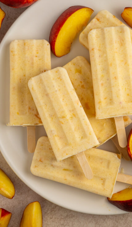 A white plate with fresh peach slices and frozen peach yogurt popsicles.
