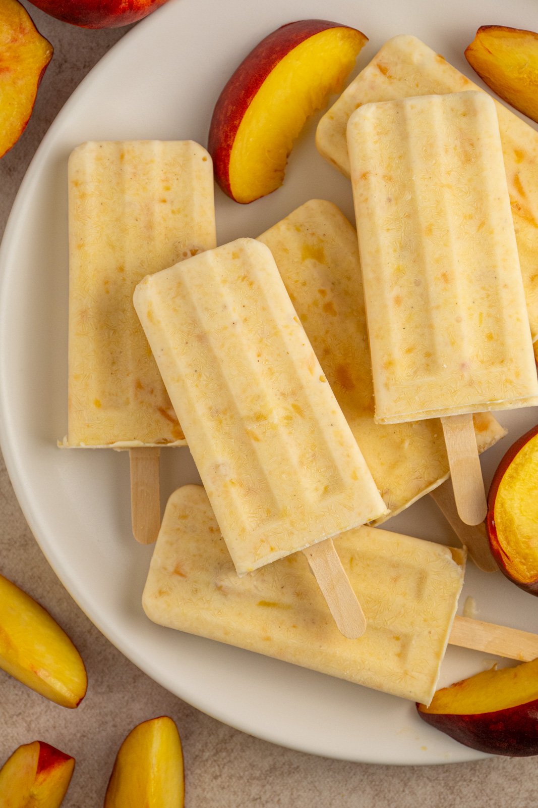 A white plate with fresh peach slices and frozen peach yogurt popsicles.