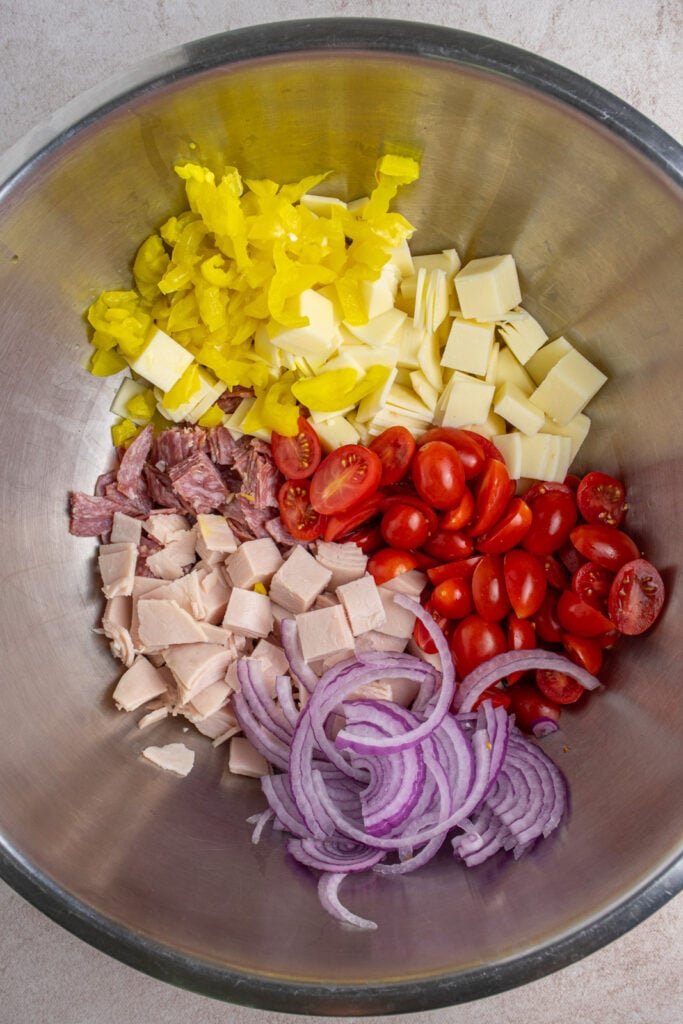 Making grinder pasta salad by adding all the chopped ingredients to a large bowl.