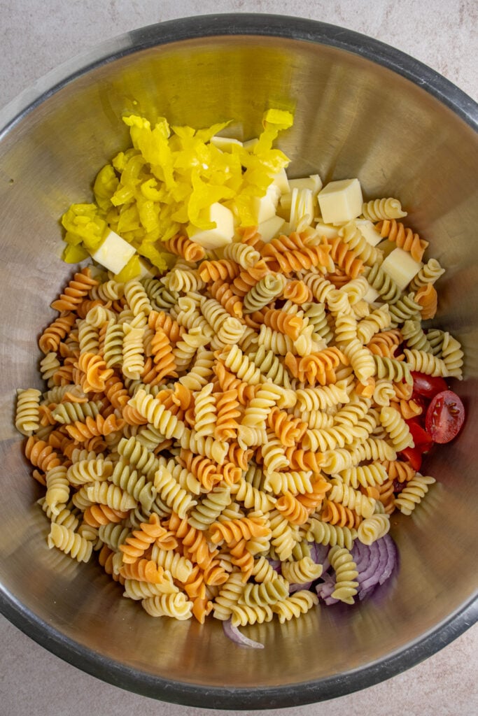 Making grinder pasta salad by adding cooked pasta to a large bowl with the other ingredients.