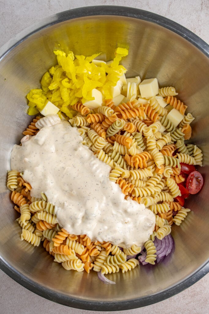 Adding dressing to a large bowl of ingredients for making grinder pasta salad.
