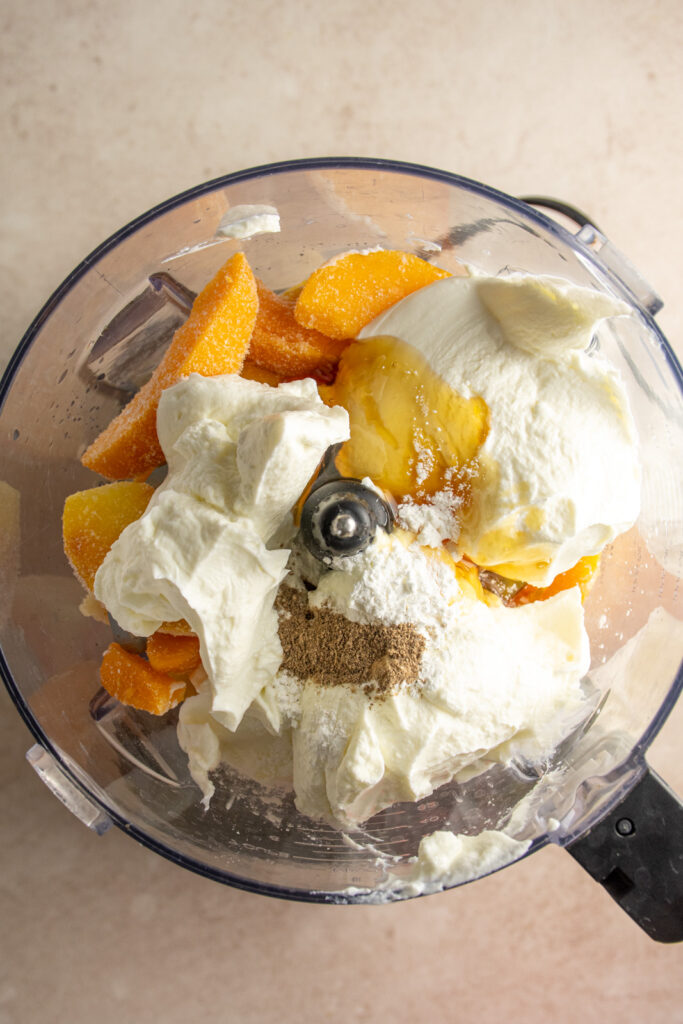 A food processor with frozen peaches, greek yogurt, and honey.