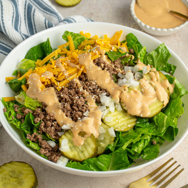 A white bowl filled with big mac salad with ground beef, pickles, cheese, and special sauce.