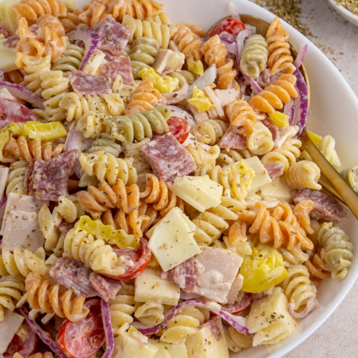 A white serving bowl filled with colorful grinder pasta salad with deli meats, cheeses, and veggies.