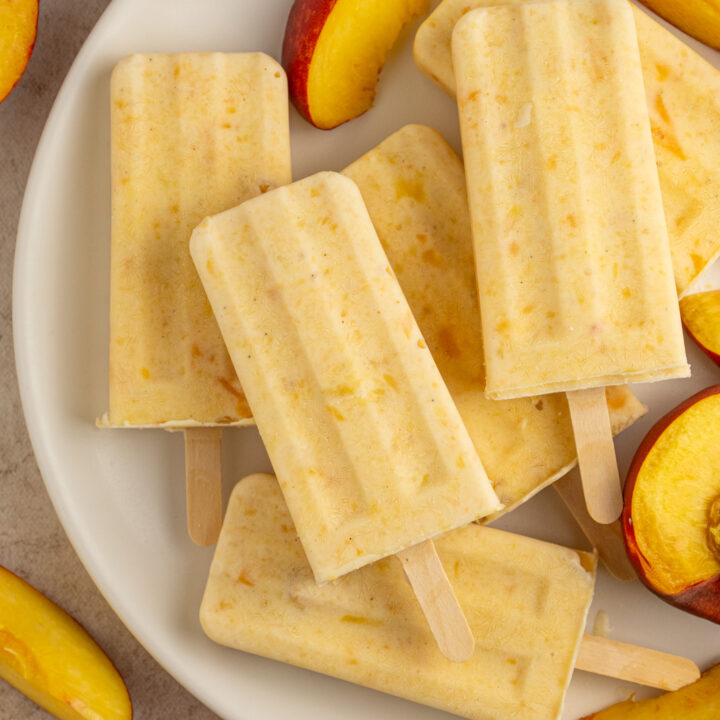A white plate full of fresh peach slices and frozen peach yogurt popsicles.