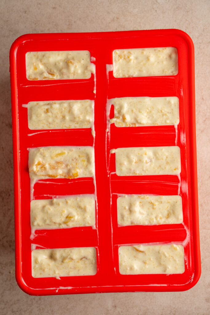 A red silicone popsicle mold filled with filling for peach yogurt popsicles.