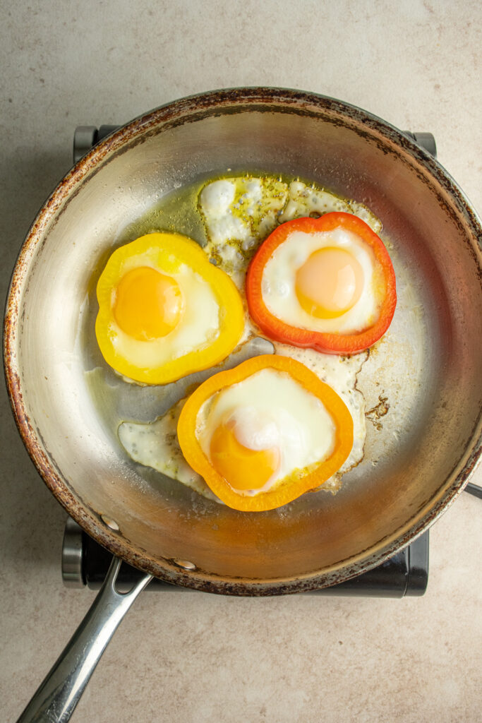 Eggs cooking in pepper rings in a skillet.
