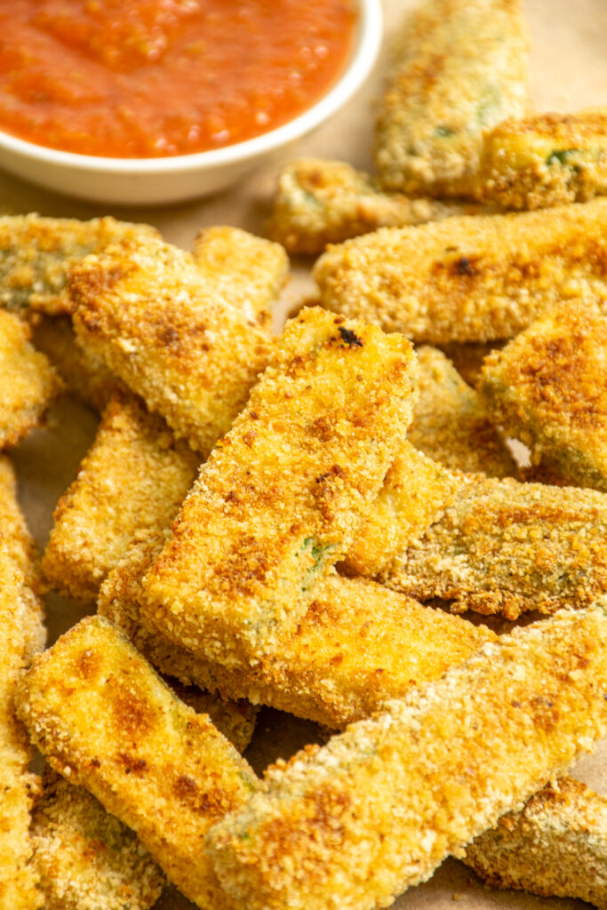 Close up of a brown and crispy zucchini fry on a platter next to some marinara sauce.