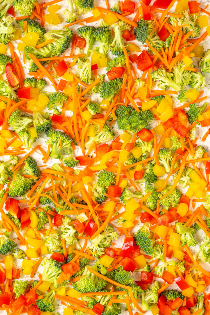 Close up of veggie pizza with dill dip covered in broccoli, carrots, and bell peppers.