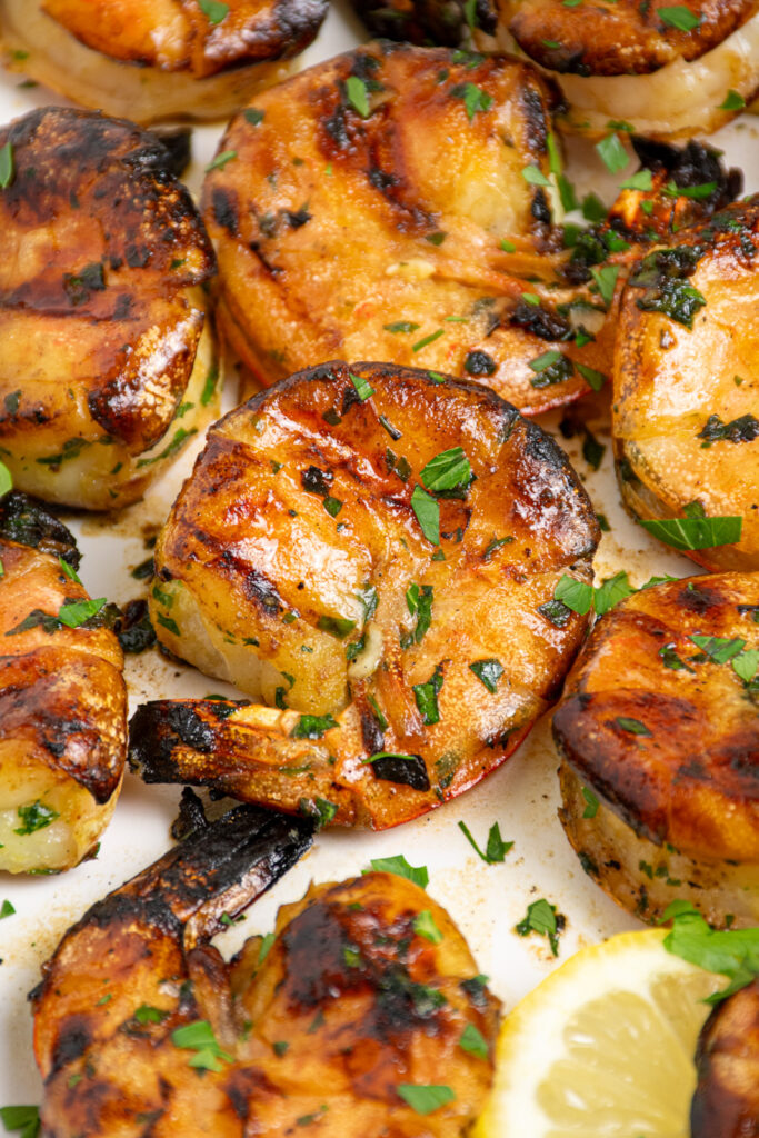 White plate filled with grilled jumbo shrimp garnished with fresh parsley.