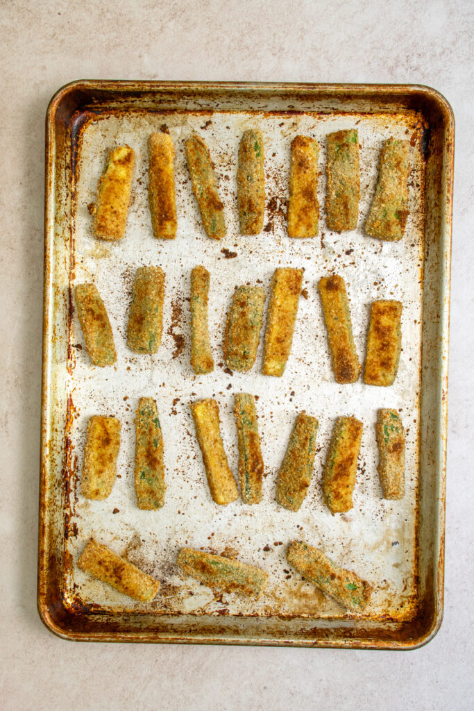 Fully cooked baked zucchini fries on a greased sheet pan.