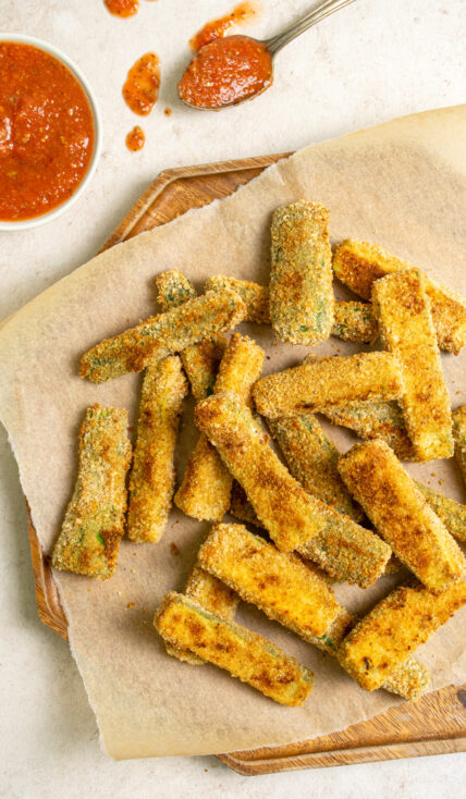 A platter of crispy oven baked zucchini fries next to a serving of marinara sauce.