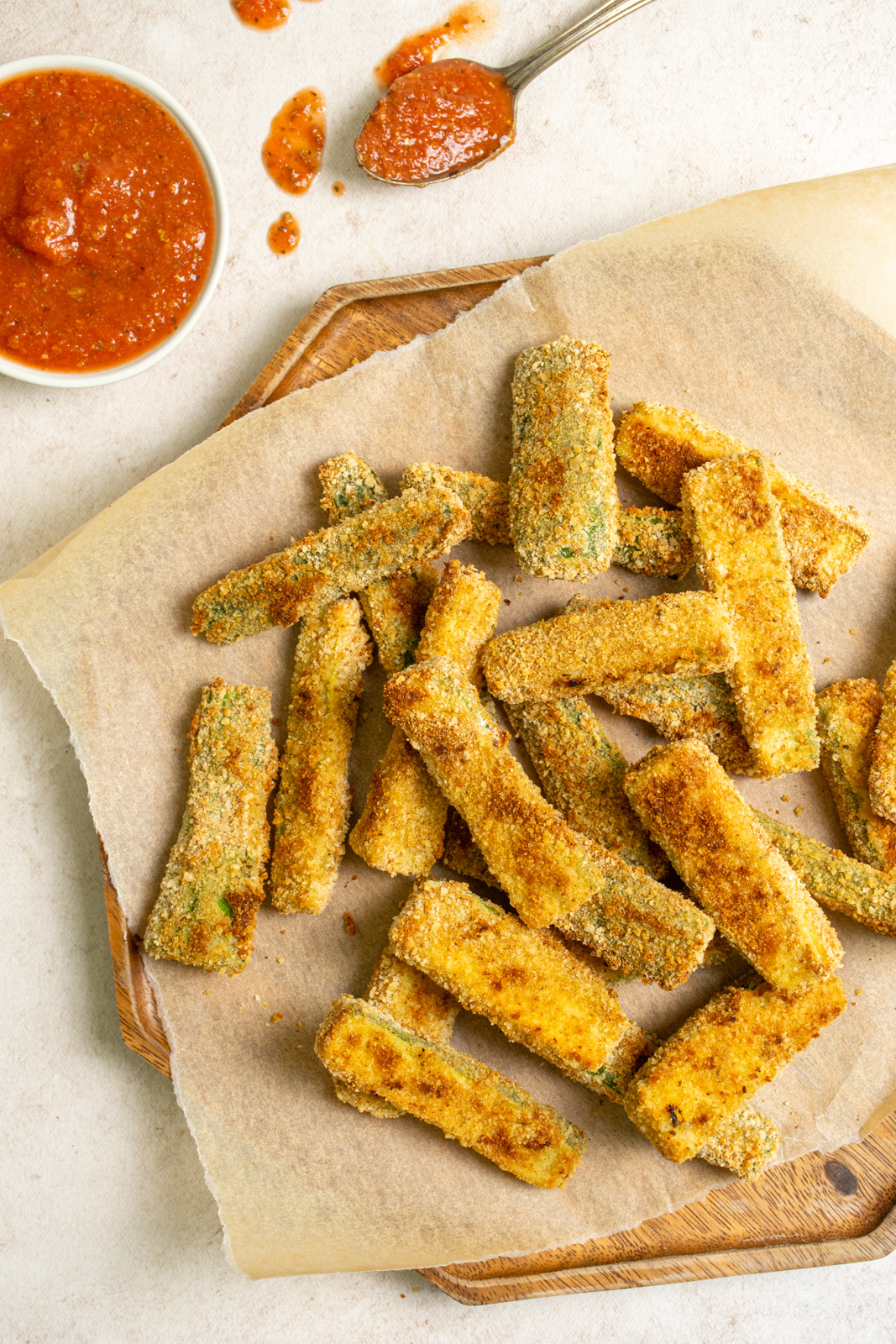 A platter of crispy oven baked zucchini fries next to a serving of marinara sauce.