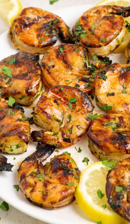 White plate filled with grilled jumbo shrimp garnished with fresh parsley.