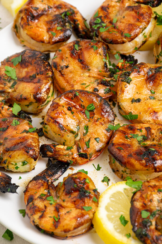 White plate filled with grilled jumbo shrimp garnished with fresh parsley.