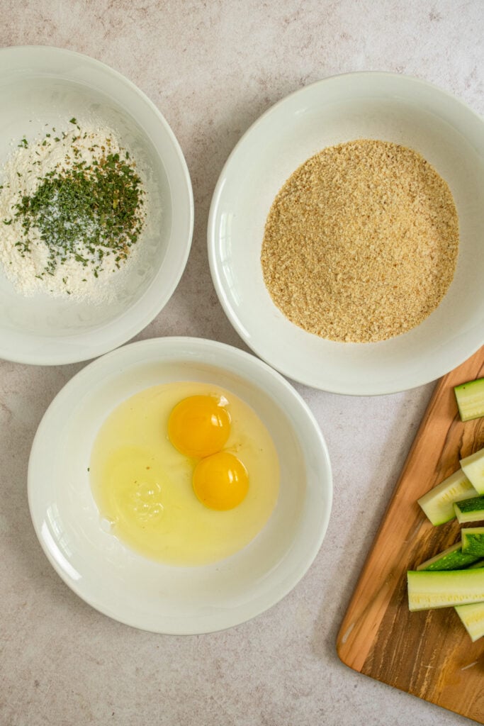 The three bowls of flour, eggs, and breadcrumbs for breading the zucchini.