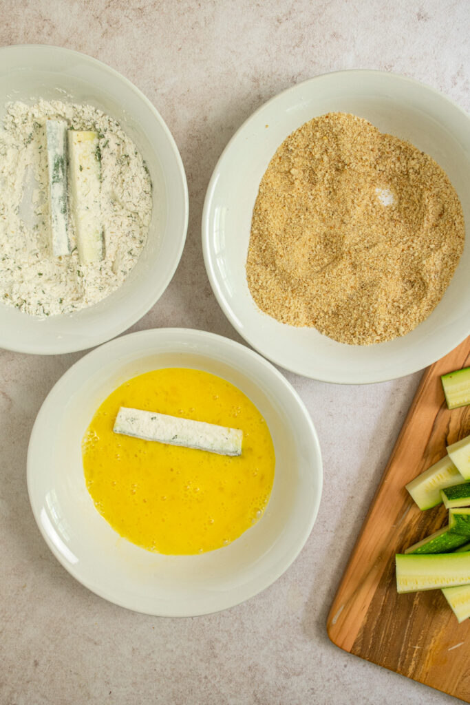 Dipping a zucchini fry in the beaten eggs.